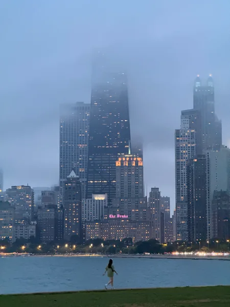 A waterfront skyline disappears into blue fog, with a lone figure beside the water.