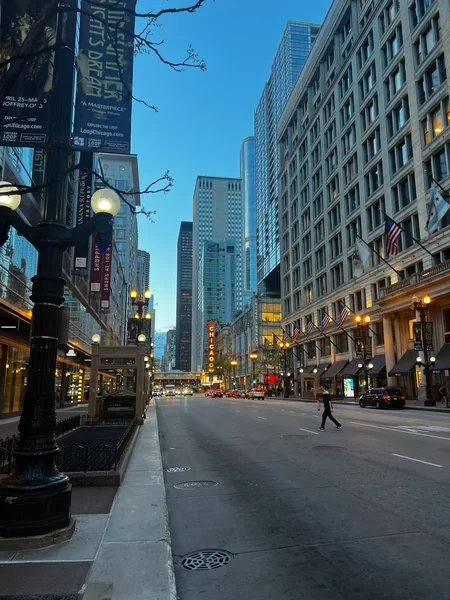 An ornate street clock stands beside a city street lined with tall buildings.