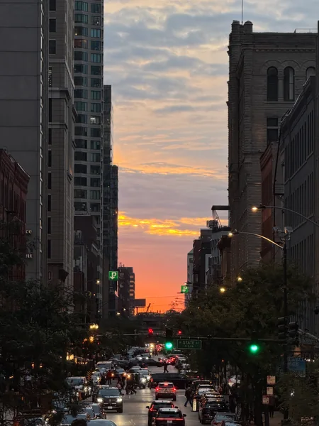 An orange sunset glows between buildings above a busy city street.