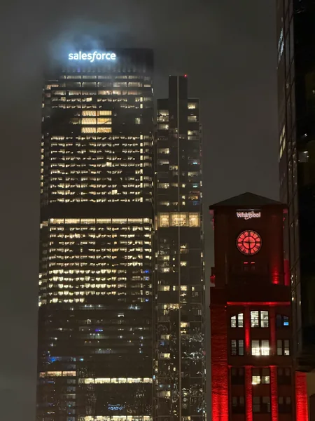 Illuminated high-rise windows and red signage shine through a dark, hazy evening.