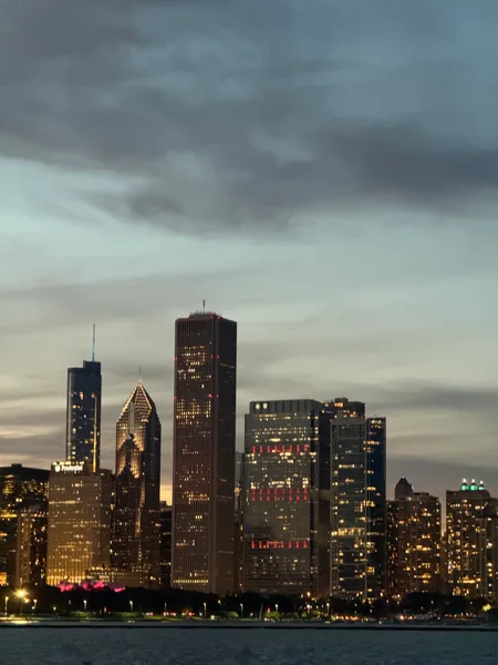 Clouds gather above an illuminated waterfront skyline at dusk.