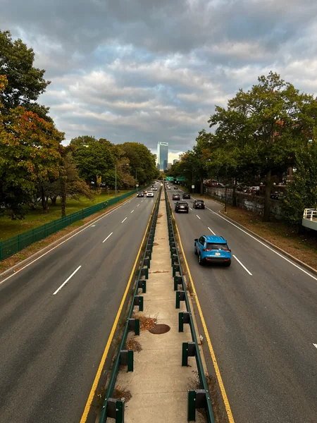 Cars travel along a tree-lined divided road seen from above.