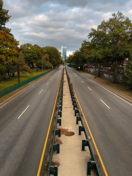A quiet divided road extends between green trees beneath gathering clouds.